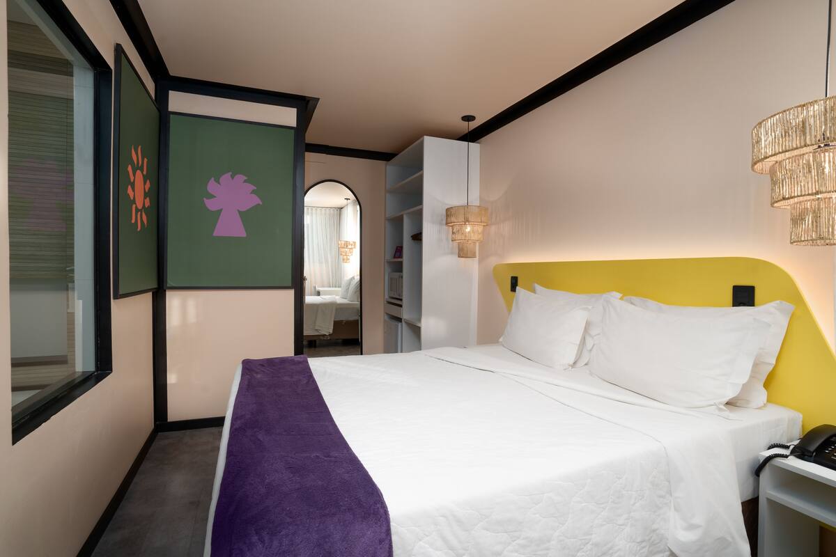 A hotel room with a bed, a desk, a phone, and a window.