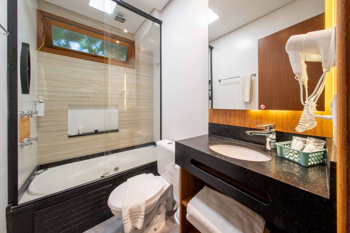 A modern bathroom with a glass-enclosed shower, a bathtub, a sink with a mirror, and a hairdryer mounted on the wall.