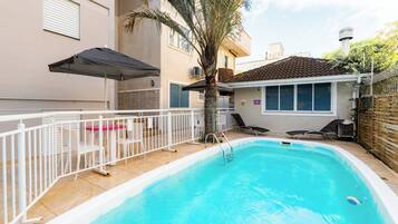 Une piscine entourée d’une clôture blanche, avec un palmier et des chaises longues.