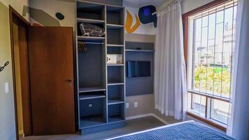 Ein Schlafzimmer mit einem Bett, Einbauschränken, einem Fernseher und einem Fenster mit Vorhängen.