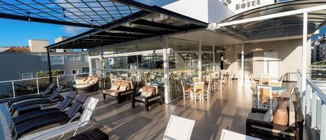 A rooftop lounge area with sun loungers, a glass-enclosed bar, and a sign for Bossa Jurê Hotel.