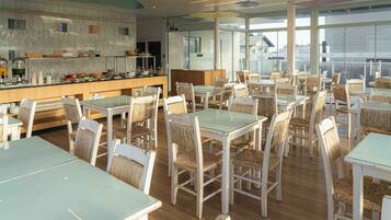 A spacious dining area with multiple tables and chairs, a counter with food items, and large windows providing natural light.