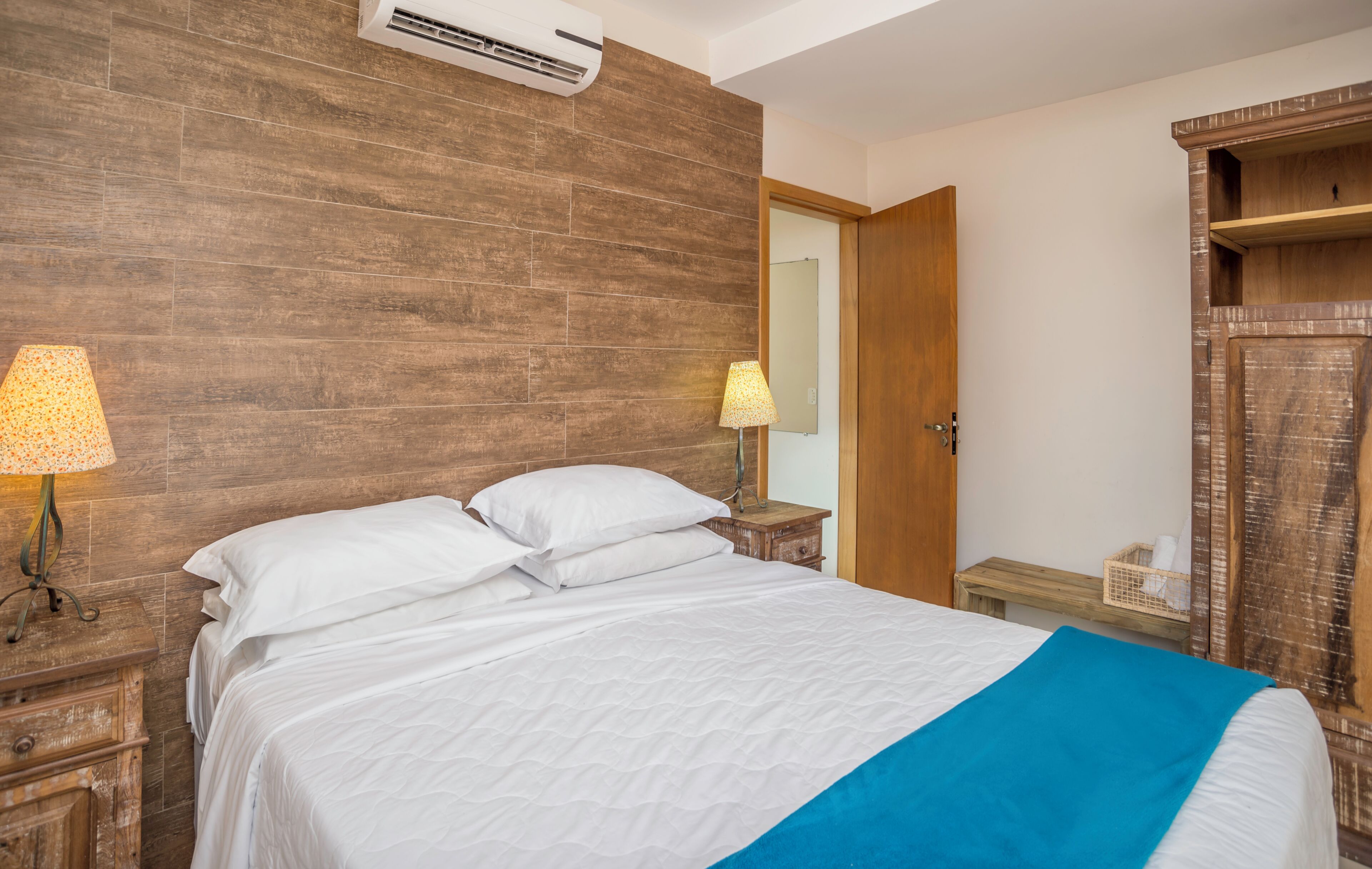 A bedroom with a wooden headboard, a bed with white bedding, a nightstand with a lamp, and a wooden wardrobe.
