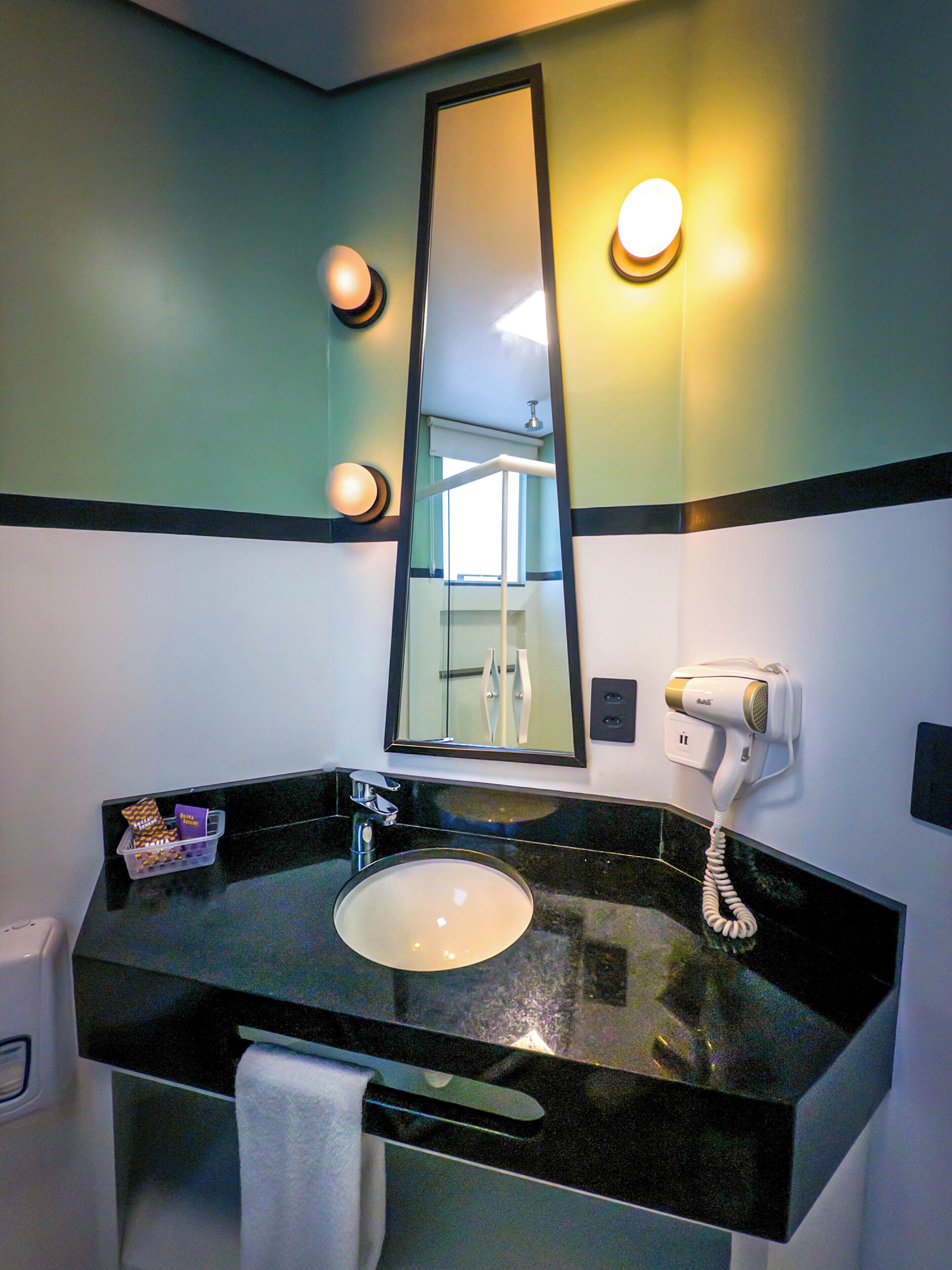 A bathroom with a round sink, a mirror, a hairdryer, and a towel rack.