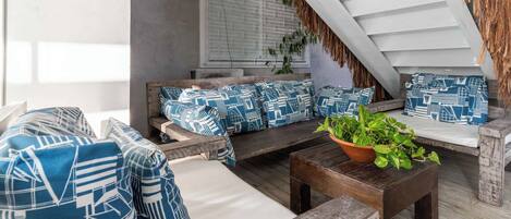 A cozy outdoor seating area with a wooden bench, a cushioned sofa with patterned cushions, and a potted plant.