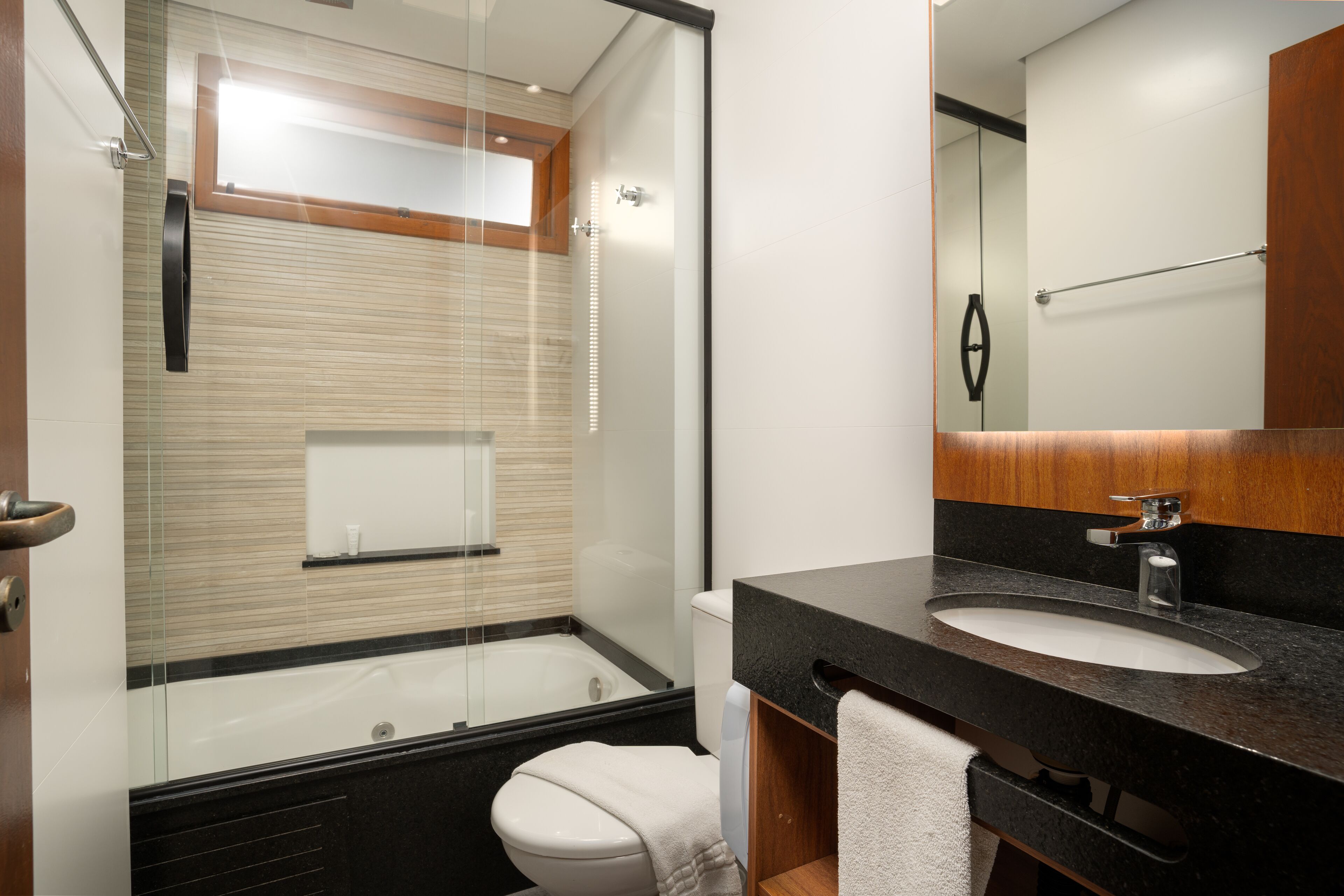A modern bathroom with a glass-enclosed shower, a white toilet, and a black countertop sink.