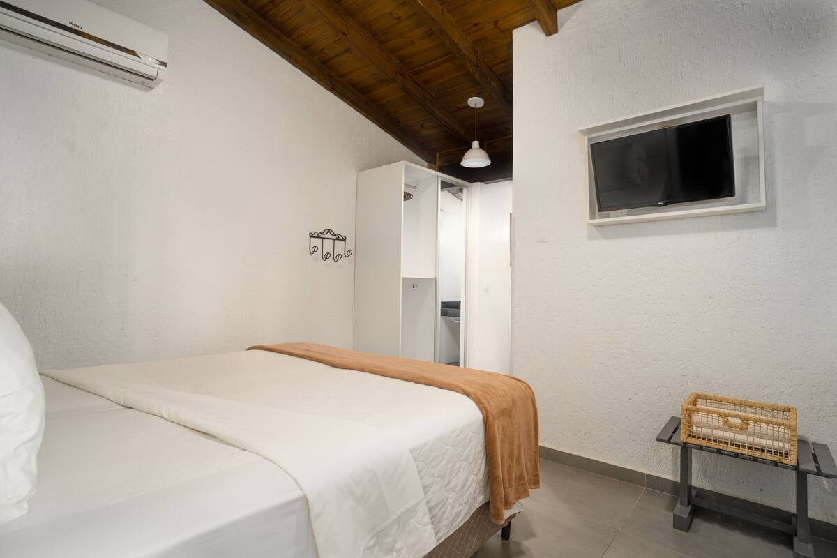 A bedroom with a bed, a window, a wardrobe, and a small table with a basket.