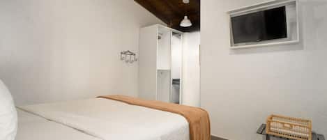 A bedroom with a bed, a window, a wardrobe, and a small table with a basket.