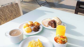 A table with breakfast items including eggs, croissants, and a muffin, along with a cup of coffee and a glass of orange juice.