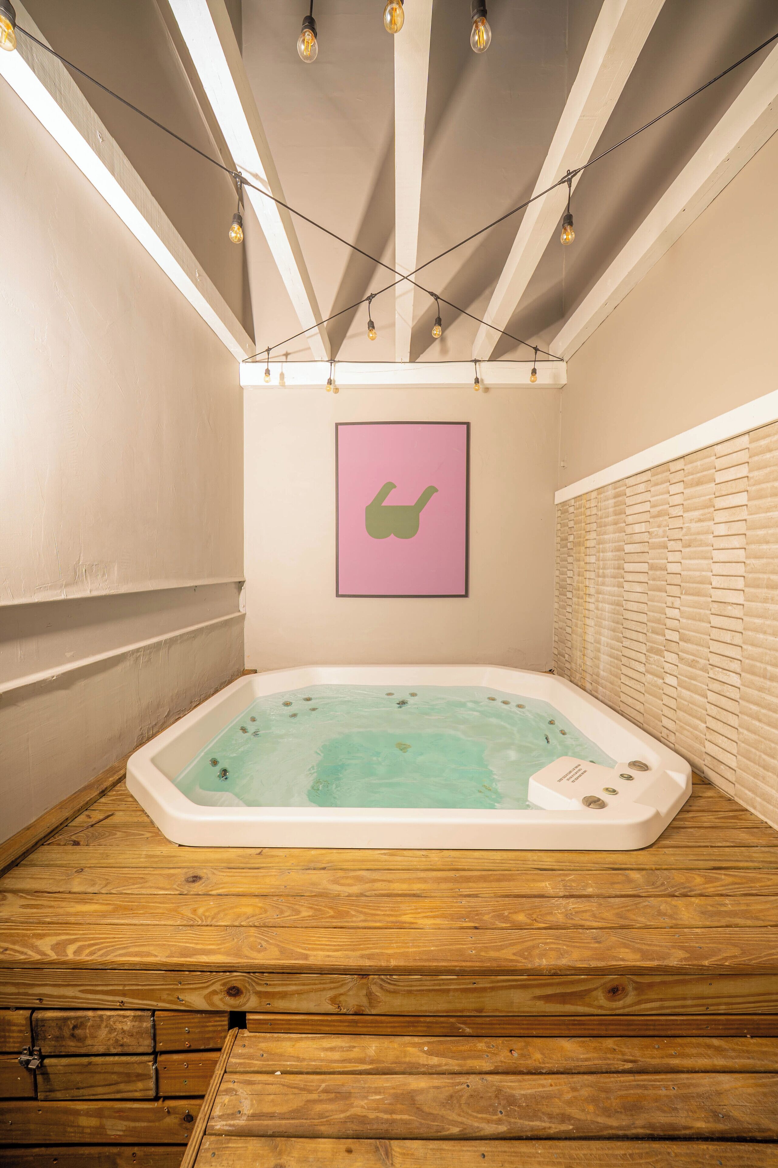 A wooden floor, a white bathtub with a green wall decal, and string lights.