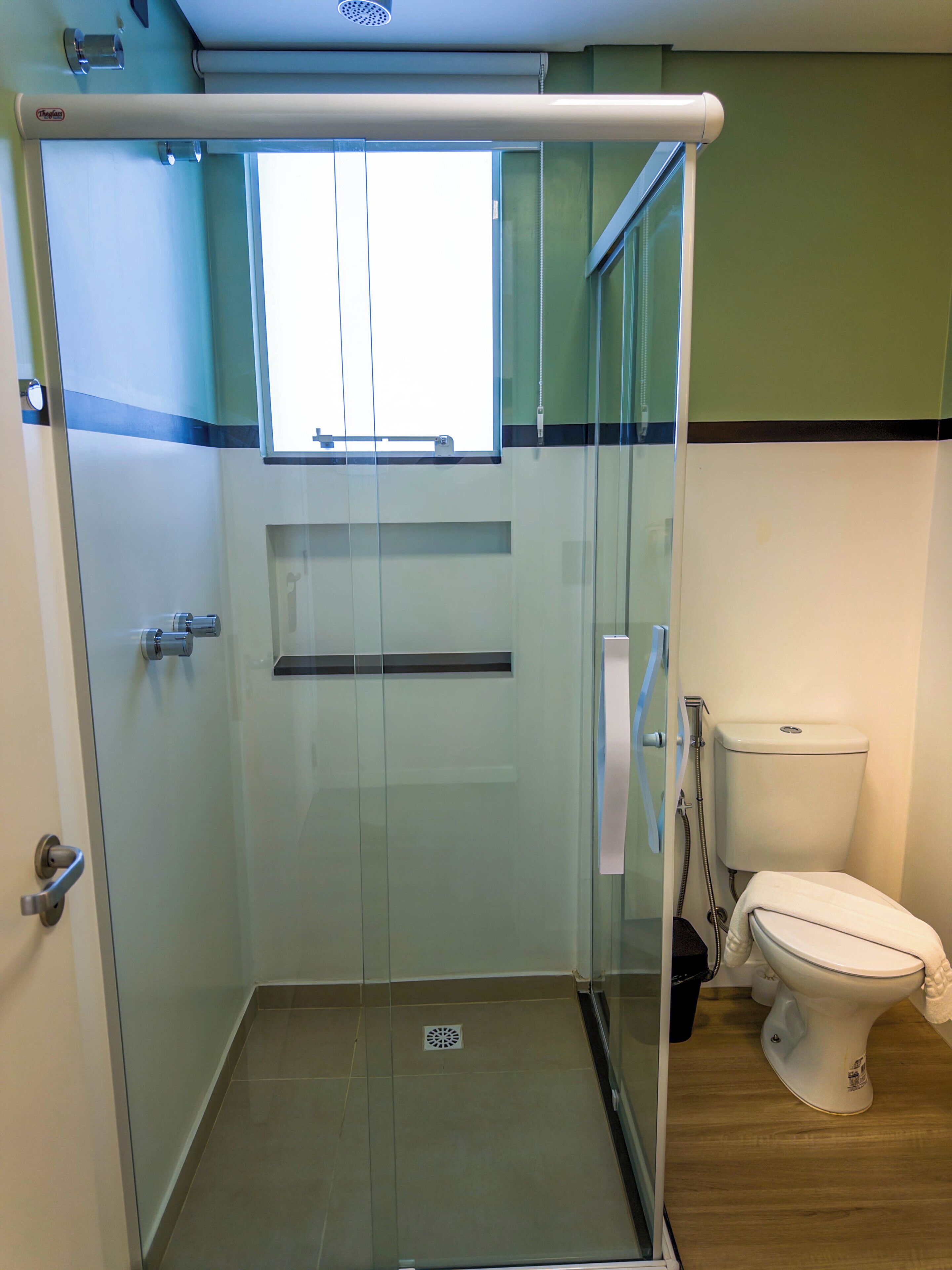 A glass-enclosed shower stall with a window, a toilet, and a sink.