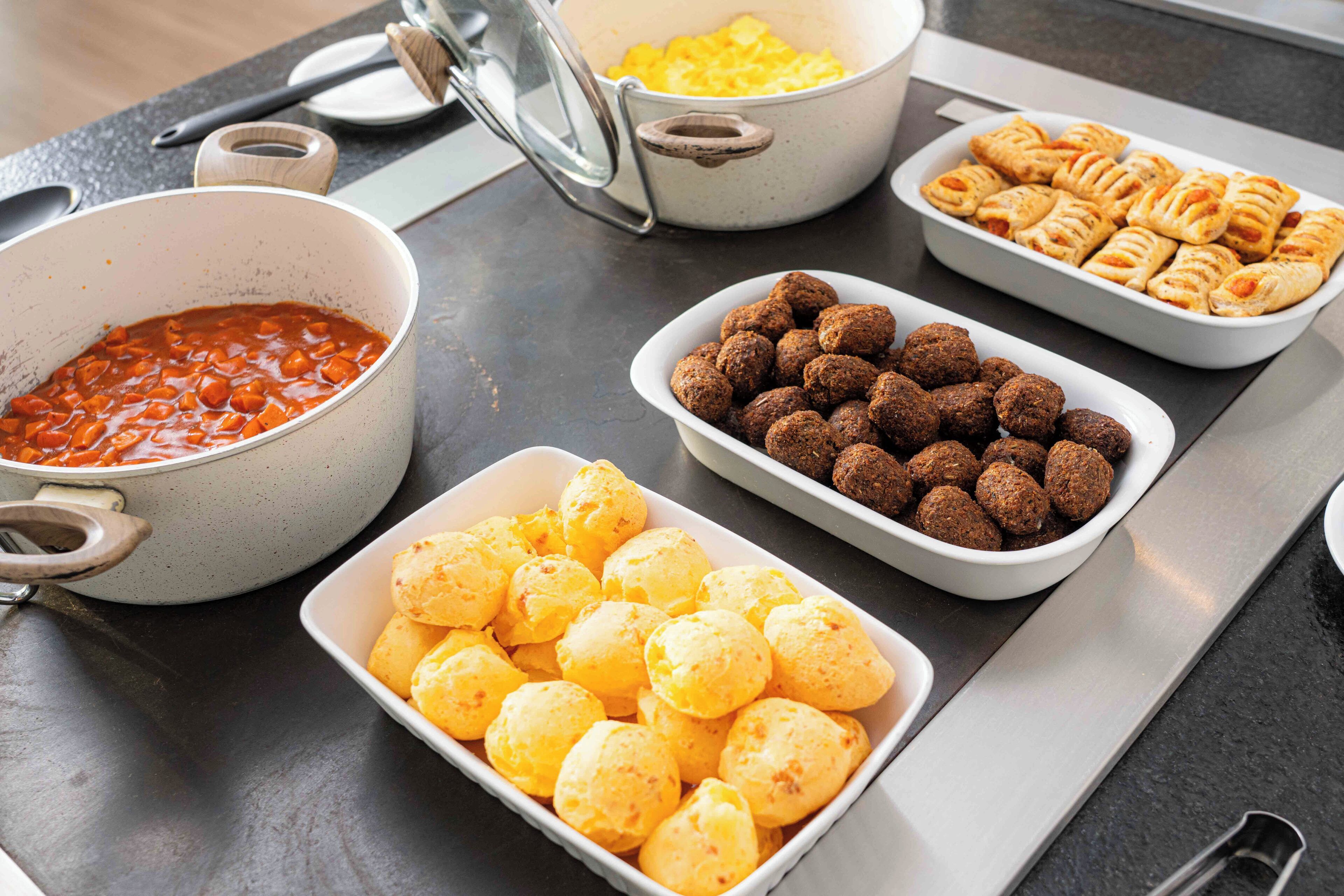 Una mesa de bufé con diferentes platos, incluyendo una olla de chili, un bol de bolitas de queso y una bandeja de albóndigas.