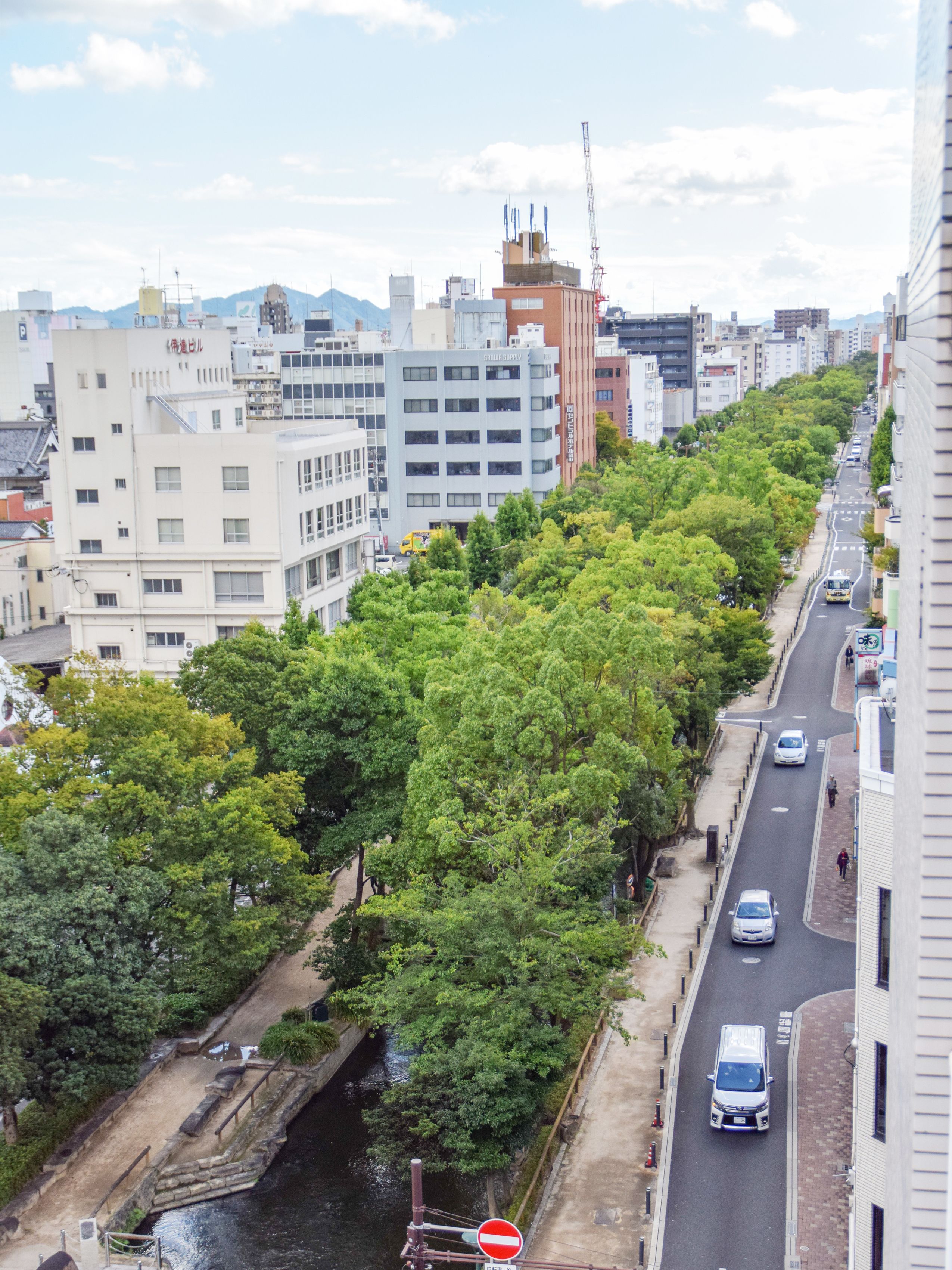 Une rue de la ville bordée d’arbres et de bâtiments, avec notamment un panneau indiquant l’interdiction de circuler et une rivière.