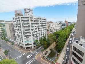 Un immeuble à plusieurs étages, dont le rez-de-chaussée est occupé par des commerces, situé à proximité d’une rivière et relié à celle-ci par un pont piétonnier.