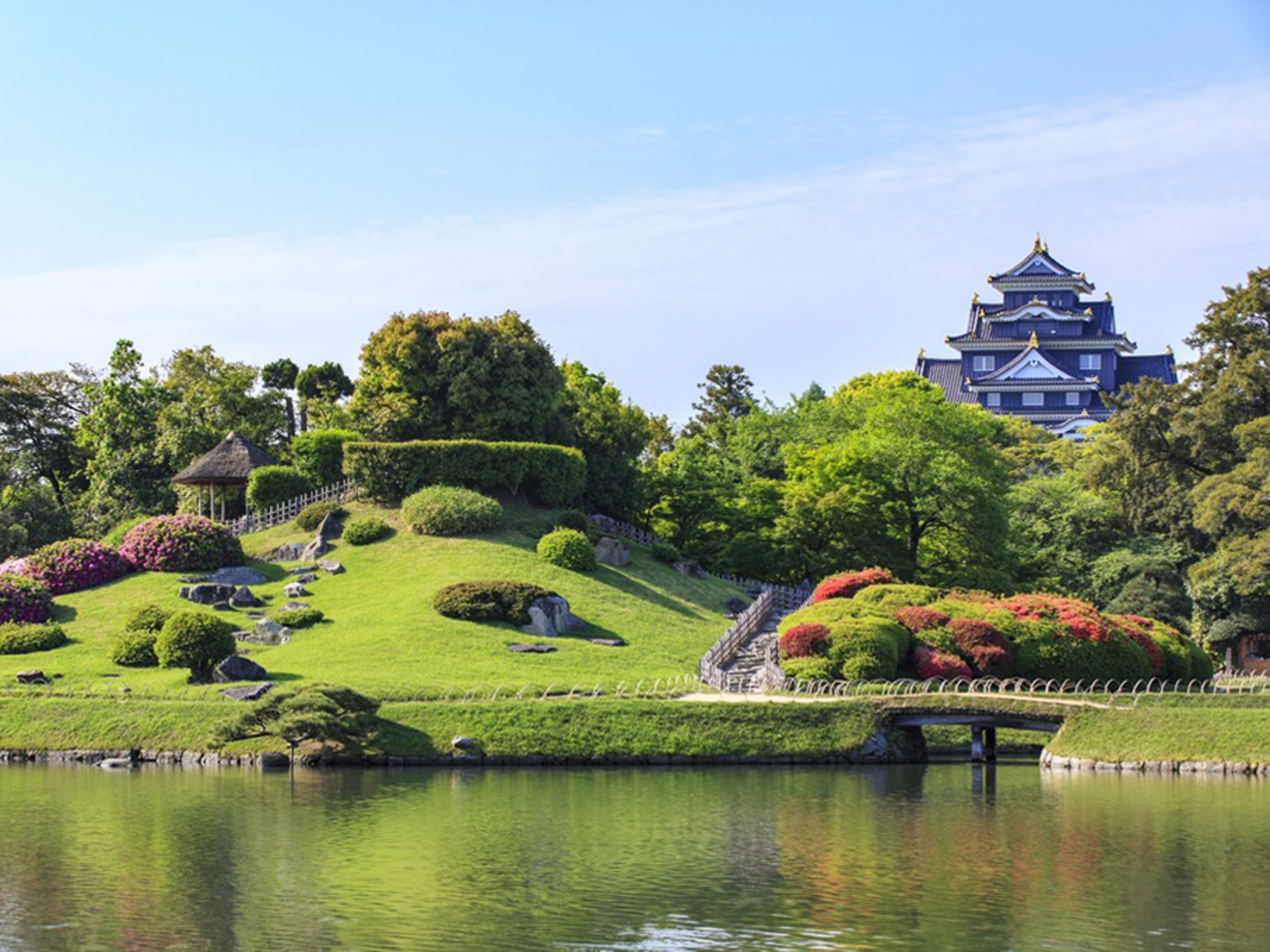 Een traditioneel Japans kasteel met een fraai onderhouden tuin, een vijver en een stenen brug.