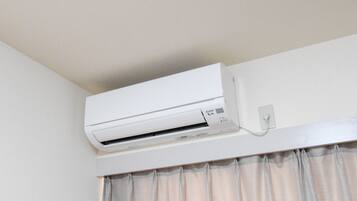 Eine weiße Klimaanlage an einer Wand über einem Fenster mit hellen Vorhängen.