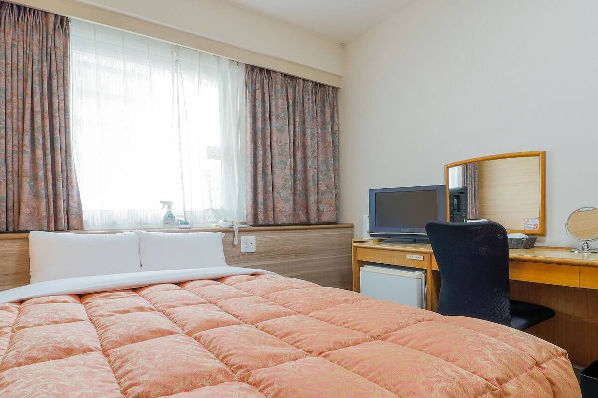 Quarto de hotel com uma cama grande, uma mesa com computador, uma cadeira e um espelho.