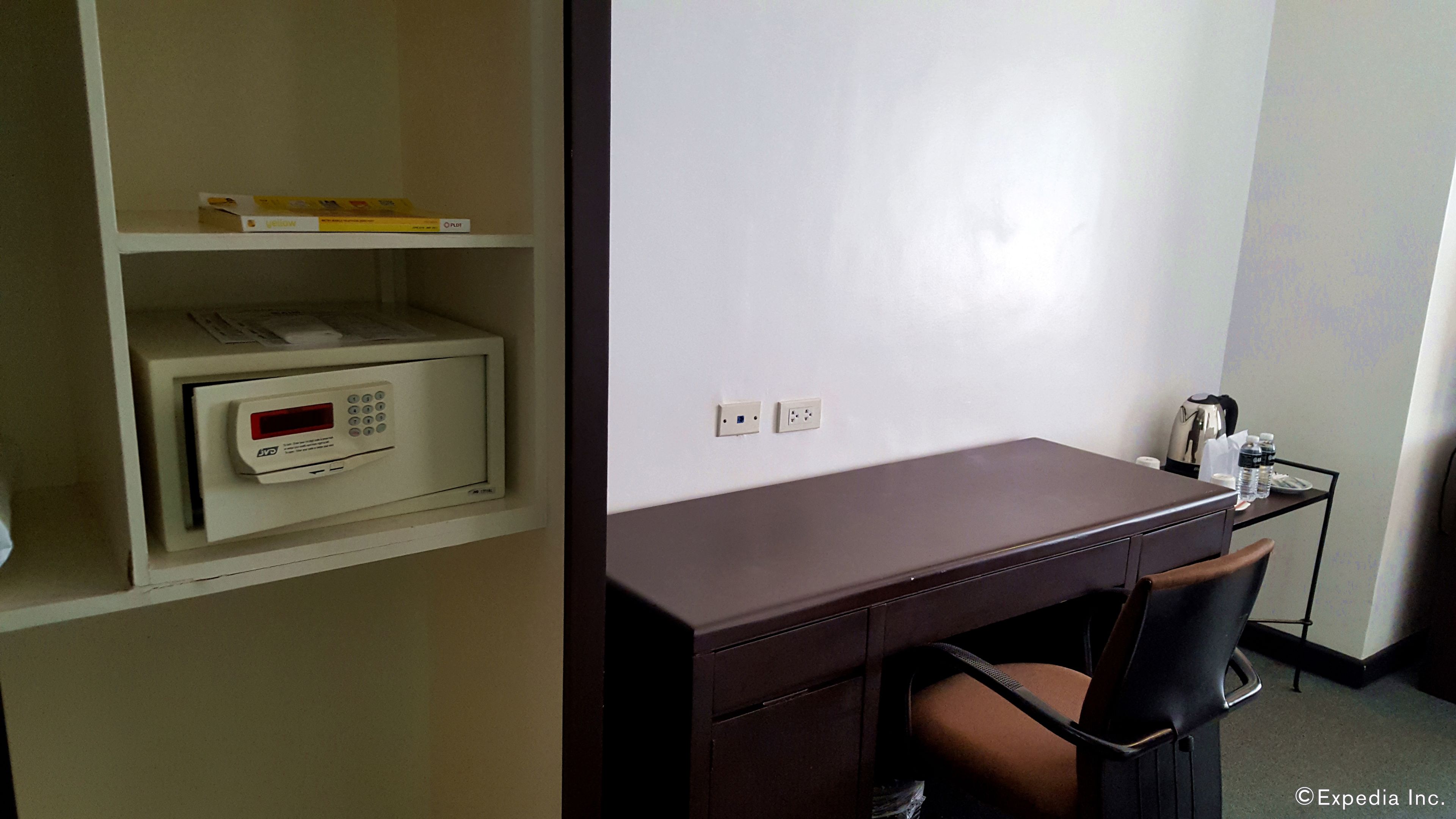 A hotel room with a desk, chair, and a microwave on a shelf.