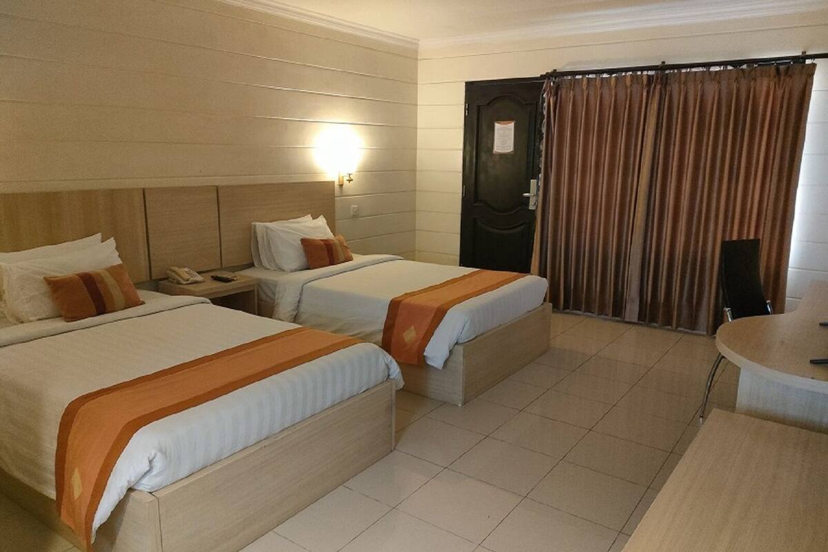 Habitación de hotel con dos camas, un escritorio, una silla y una cortina.