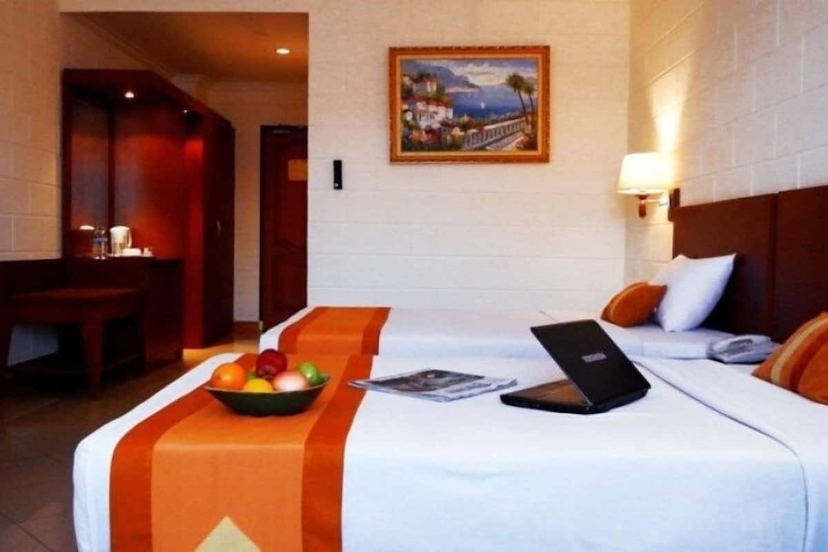Habitación de hotel con cama, escritorio, televisión, un cuadro en la pared y un frutero sobre la cama.