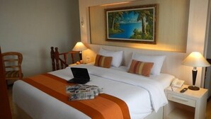 Ein Hotelzimmer mit Bett, Schreibtisch, Stuhl, einem Gemälde an der Wand und einem Laptop auf dem Bett.
