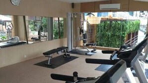 Ein Fitnessraum mit Trainingsgeräten, einem großen Spiegel und Blick auf Grünflächen.