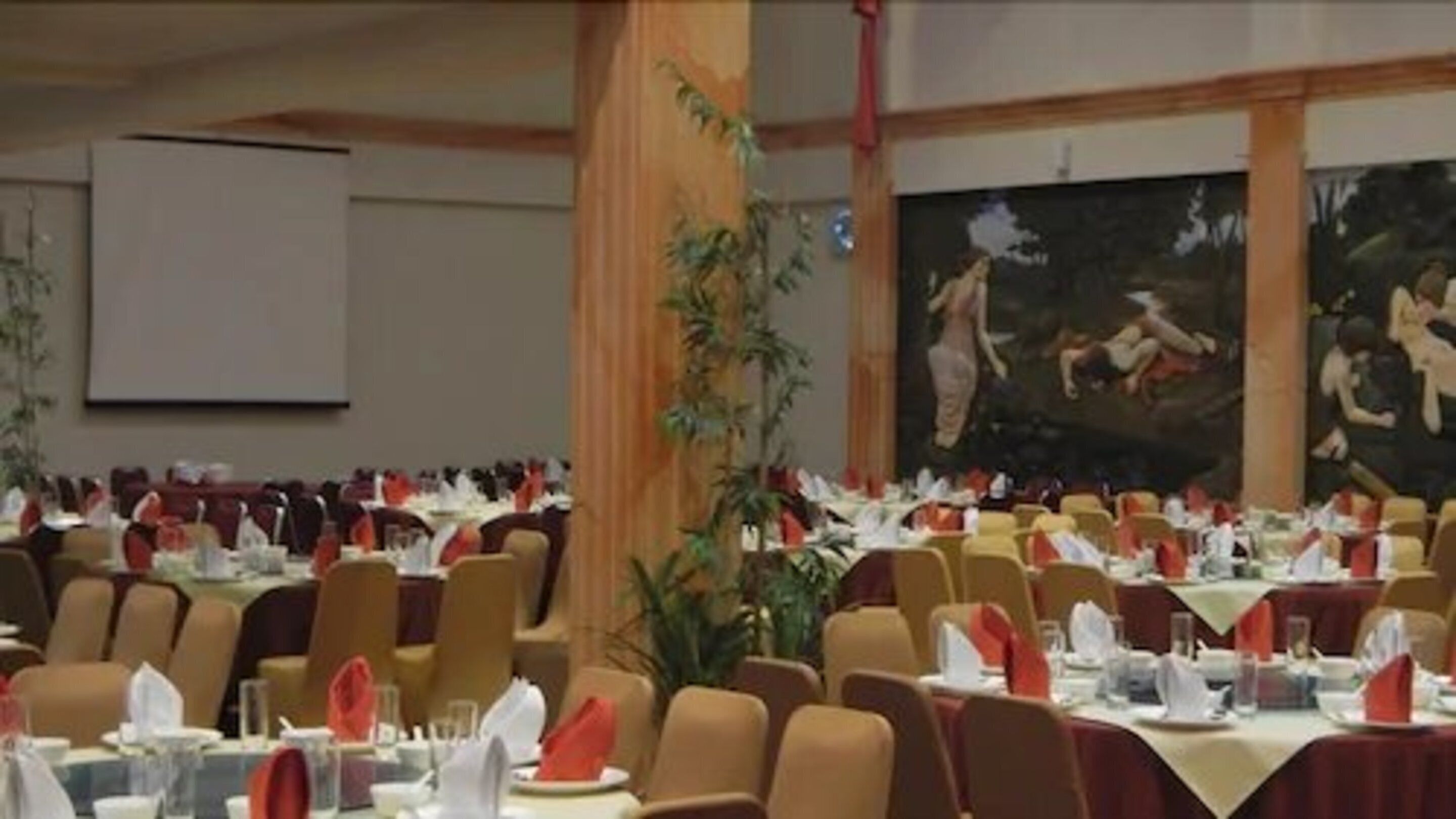A banquet hall with multiple tables set for dining, chairs arranged in rows, and a large painting on the wall.