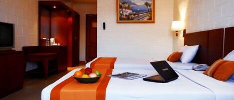A hotel room with two beds, a desk, a television, and a painting on the wall.