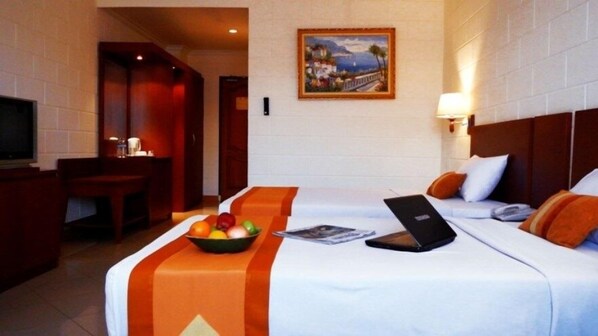 A hotel room with two beds, a desk, a television, and a painting on the wall.