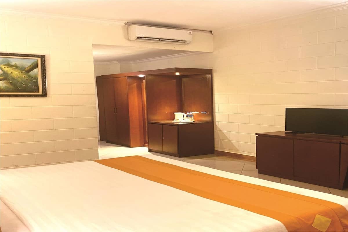 Habitación de hotel con cama, escritorio con televisor, armario y una mesita con tetera.