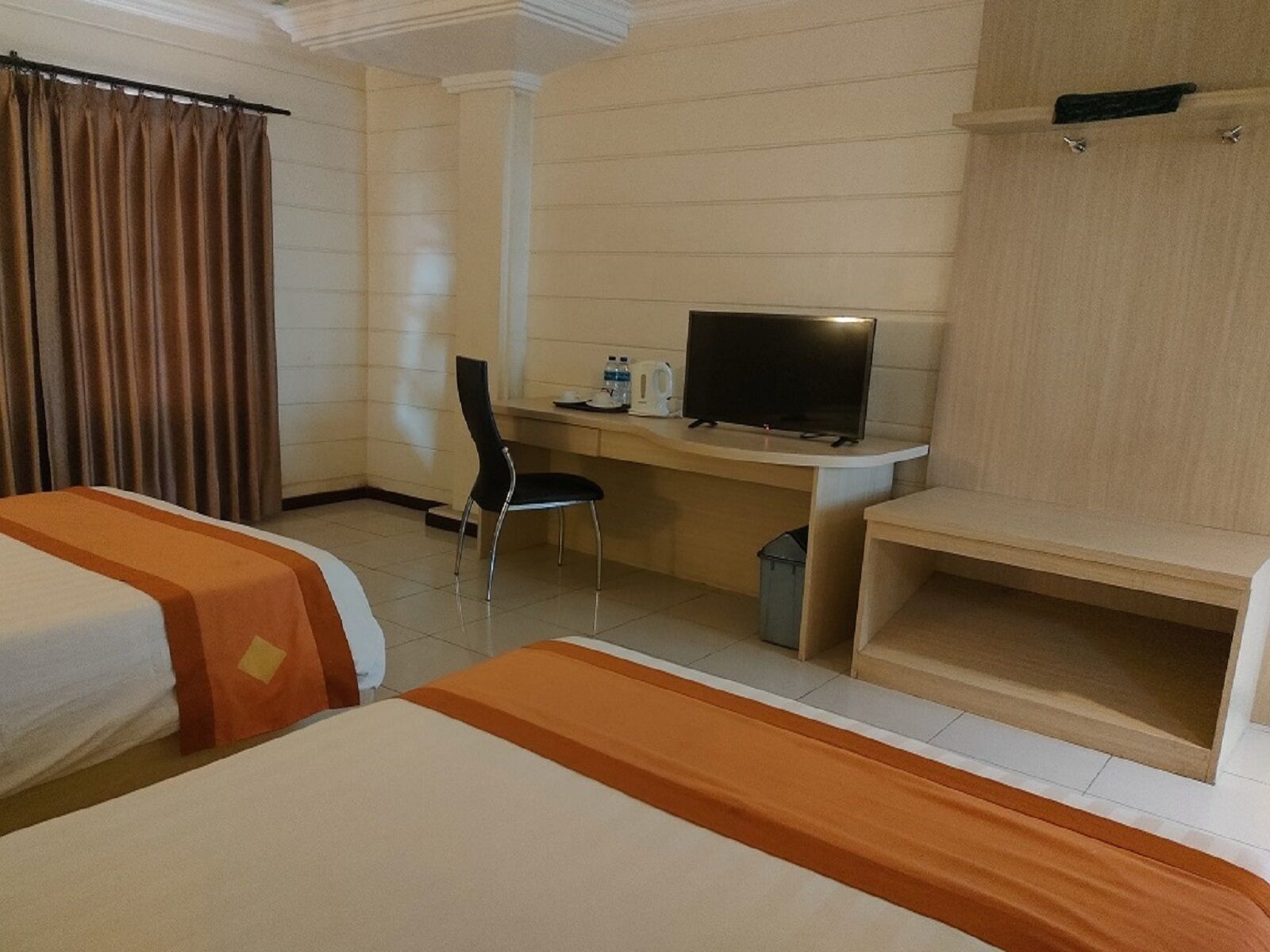 A hotel room with two beds, a desk with a television, a chair, and a small trash bin.