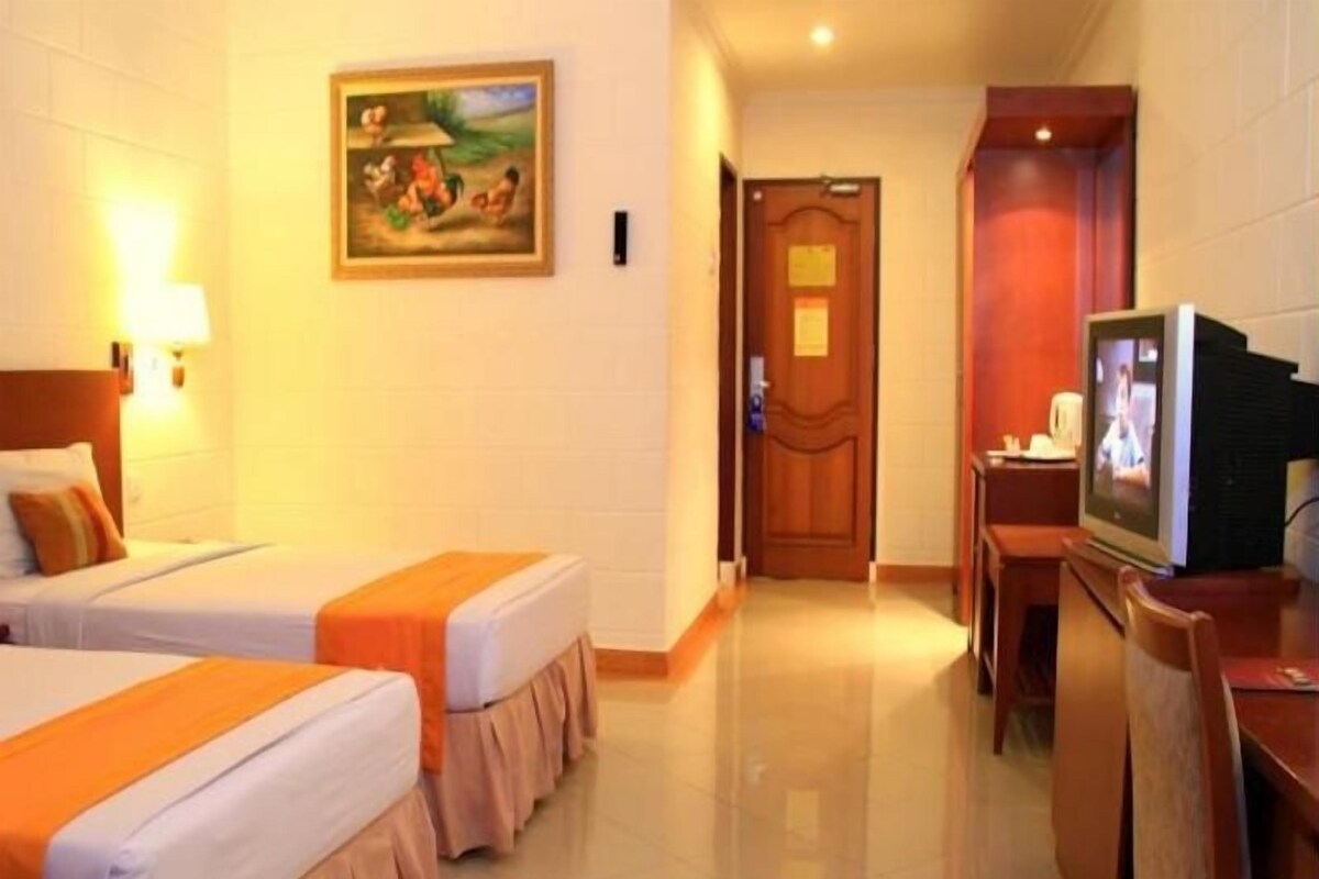 A hotel room with two beds, a television, a painting on the wall, and a door leading to another room.
