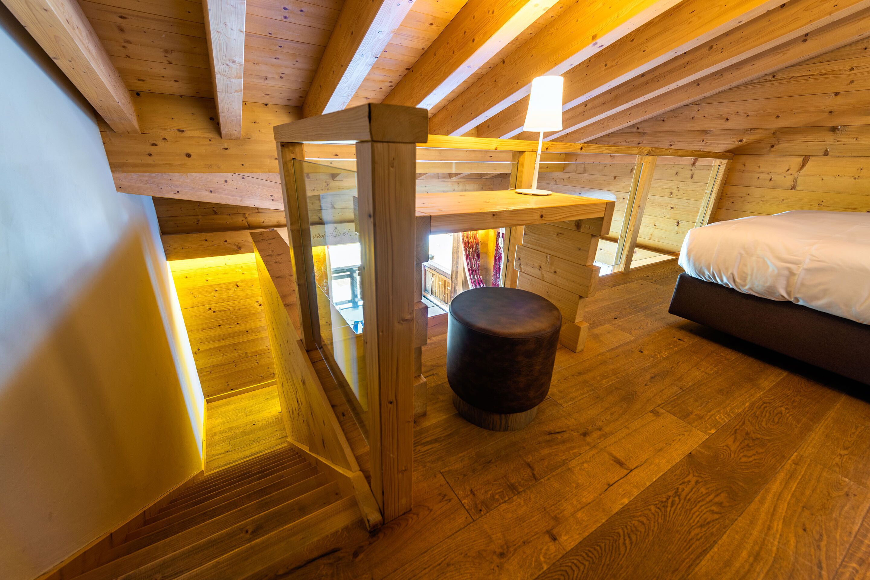Un interior de madera con una cama, un taburete pequeño y una escalera.
