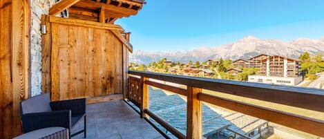 A wooden balcony with wicker furniture, overlooking a lake and mountains.