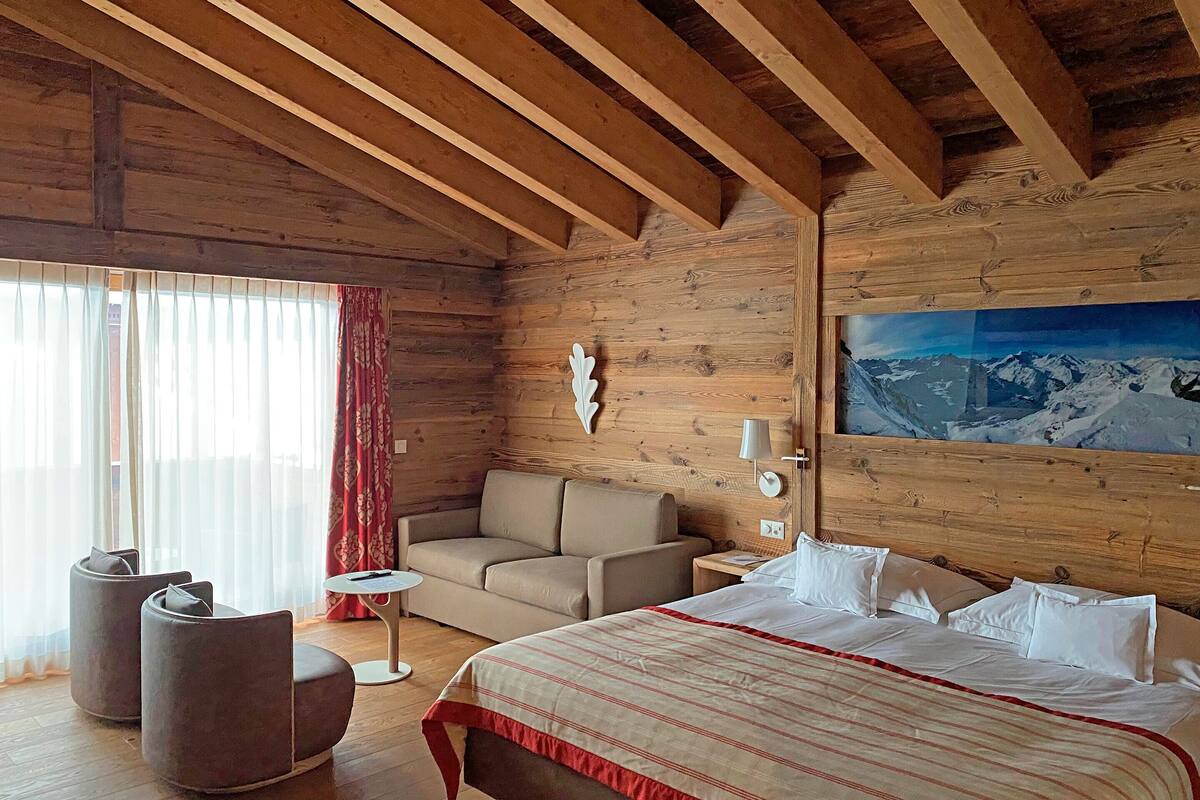 Habitación de una cabaña de madera con una cama, un sofá y dos sillones.