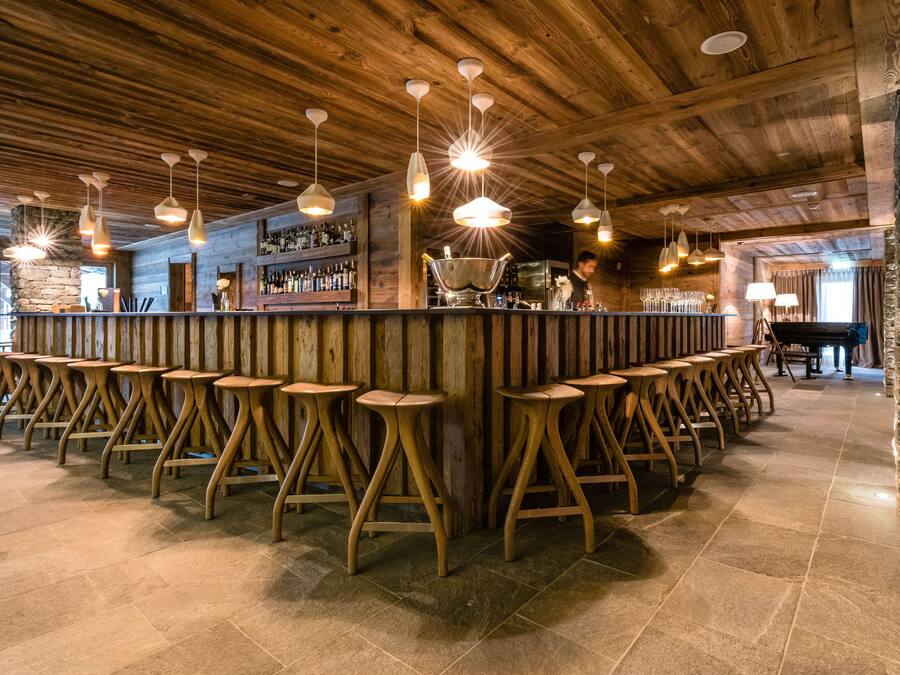 Eine Bar mit Holzhockern, hängenden Pendelleuchten und einer Steinwand.