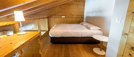 Una habitación pequeña y acogedora con techo de madera, una cama con ropa blanca, una mesita redonda y un escritorio con lámpara.