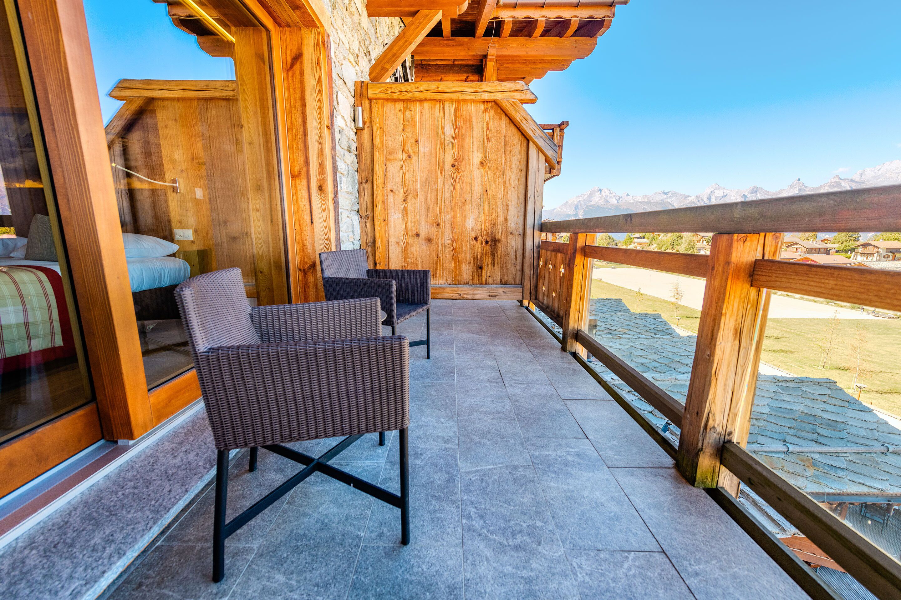 A wooden balcony with wicker chairs and a view of mountains.