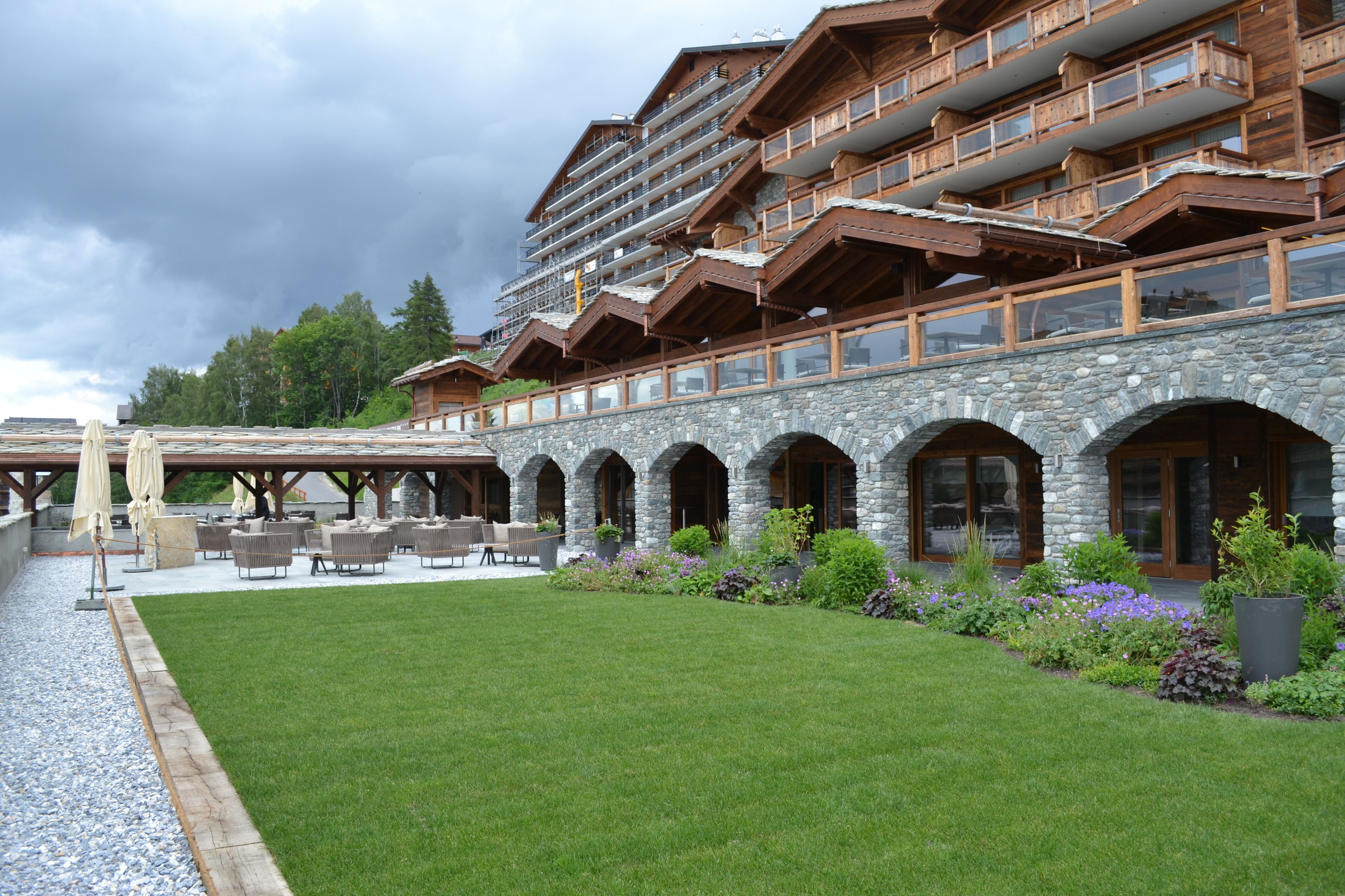 Een hotel met een gevel van natuursteen, een terras en een verzorgd gazon.