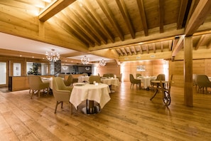A spacious dining area with wooden beams, round tables, and chairs. - Hôtel Nendaz 4 Vallées & Spa (Nendaz)