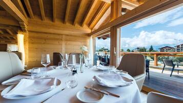 Una mesa de comedor con manteles blancos, platos y cubiertos, y vista al exterior a través de amplios ventanales.