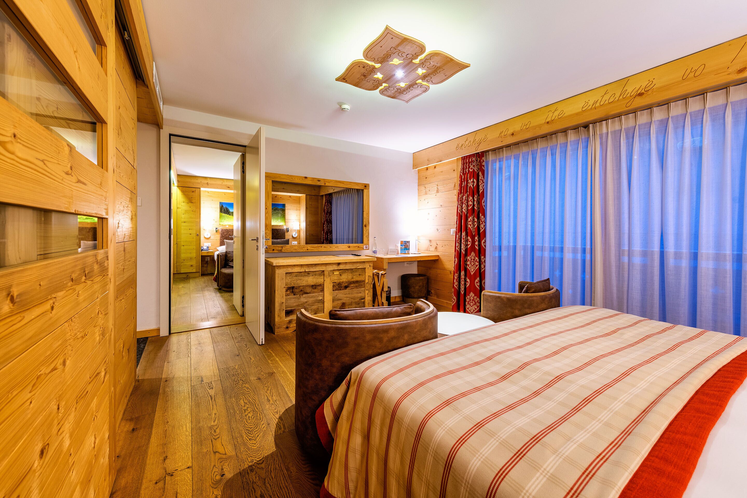 A hotel room with a wooden floor, a large bed with a striped bedspread, a wooden desk, a chair, and a mirror.
