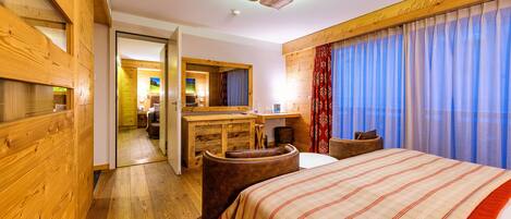 A hotel room with a wooden floor, a large bed with a striped bedspread, a wooden desk, a chair, and a mirror.