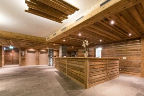 A spacious lobby with a wooden reception desk, stone pillar, and a high ceiling with exposed beams. - Hôtel Nendaz 4 Vallées & Spa (Nendaz)