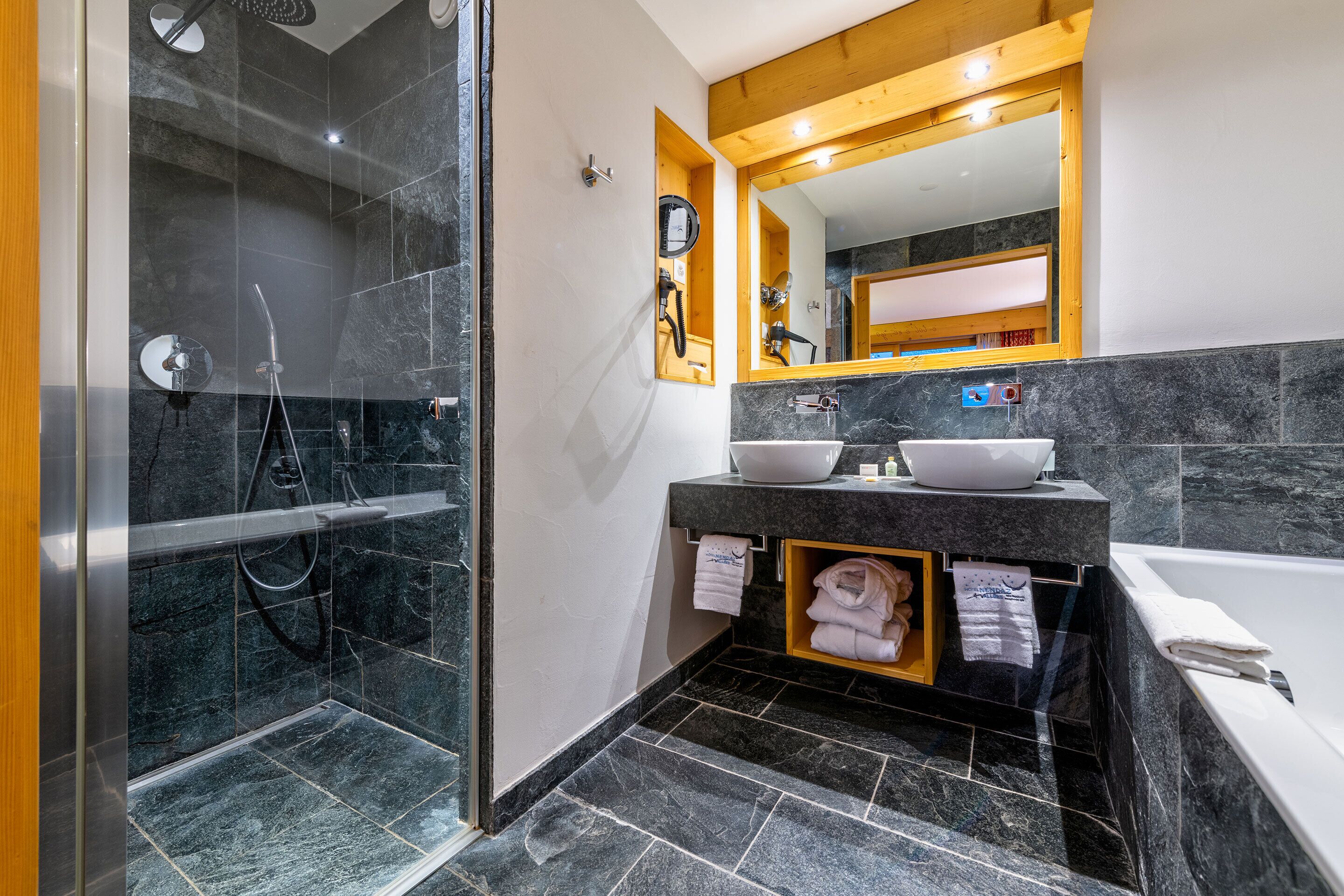 A modern bathroom with a glass-enclosed shower, a vanity with two sinks, and a bathtub.