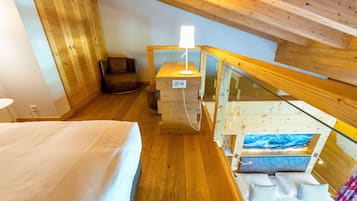 A bedroom with a bed, a nightstand, a lamp, a chair, and a glass railing.