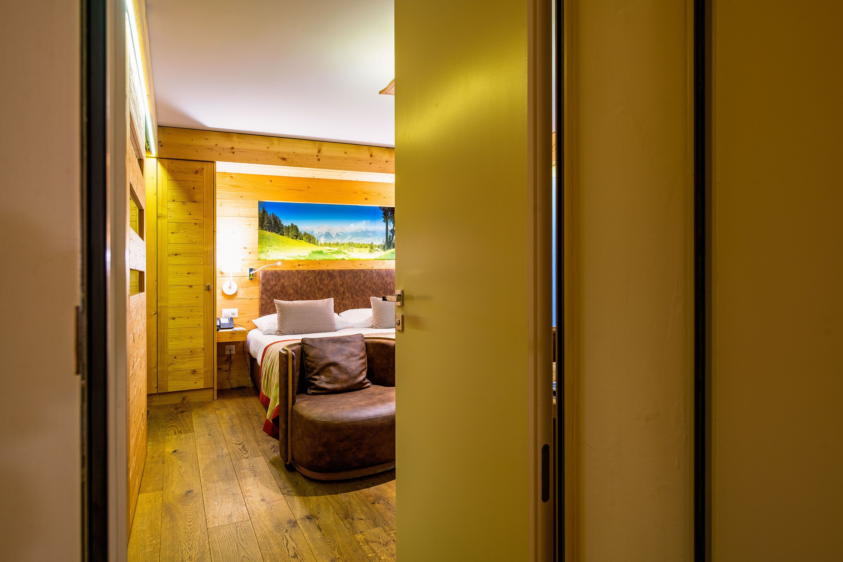 A bedroom with a wooden floor, a bed, a leather chair, and a painting of a landscape.