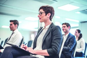 A conference room with rows of chairs and a person holding a tablet.