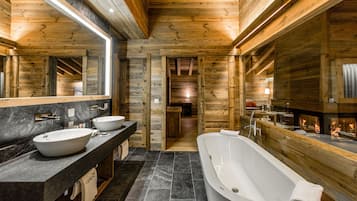 A modern bathroom with a freestanding bathtub, two sinks, and a large mirror.
