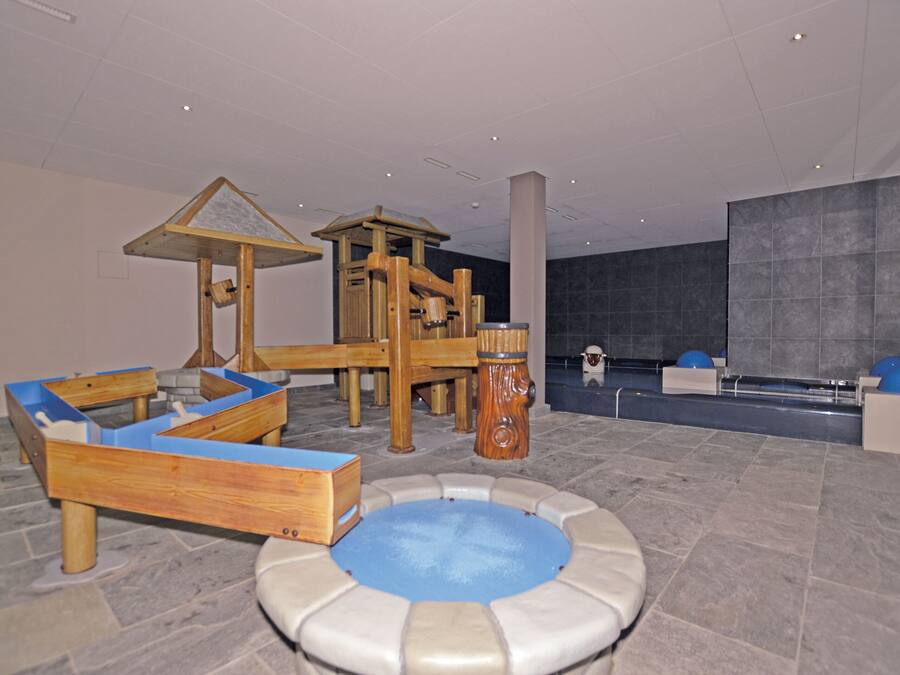 Zona infantil con una estructura de juegos de madera, una piscina pequeña y un área de descanso.